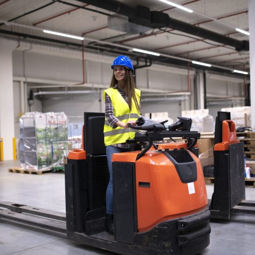 Factory worker in protective suit with hardhat driving forklift. Factory worker in protective suit with hardhat driving forklift.