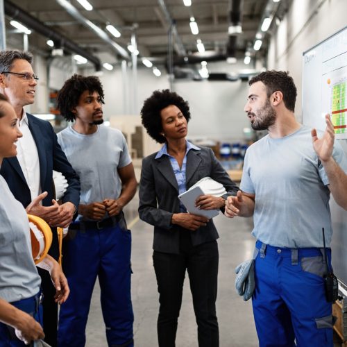 As you can see, we follow this working plan here! Young manual worker presenting new business strategy to company managers and his colleagues in a factory.